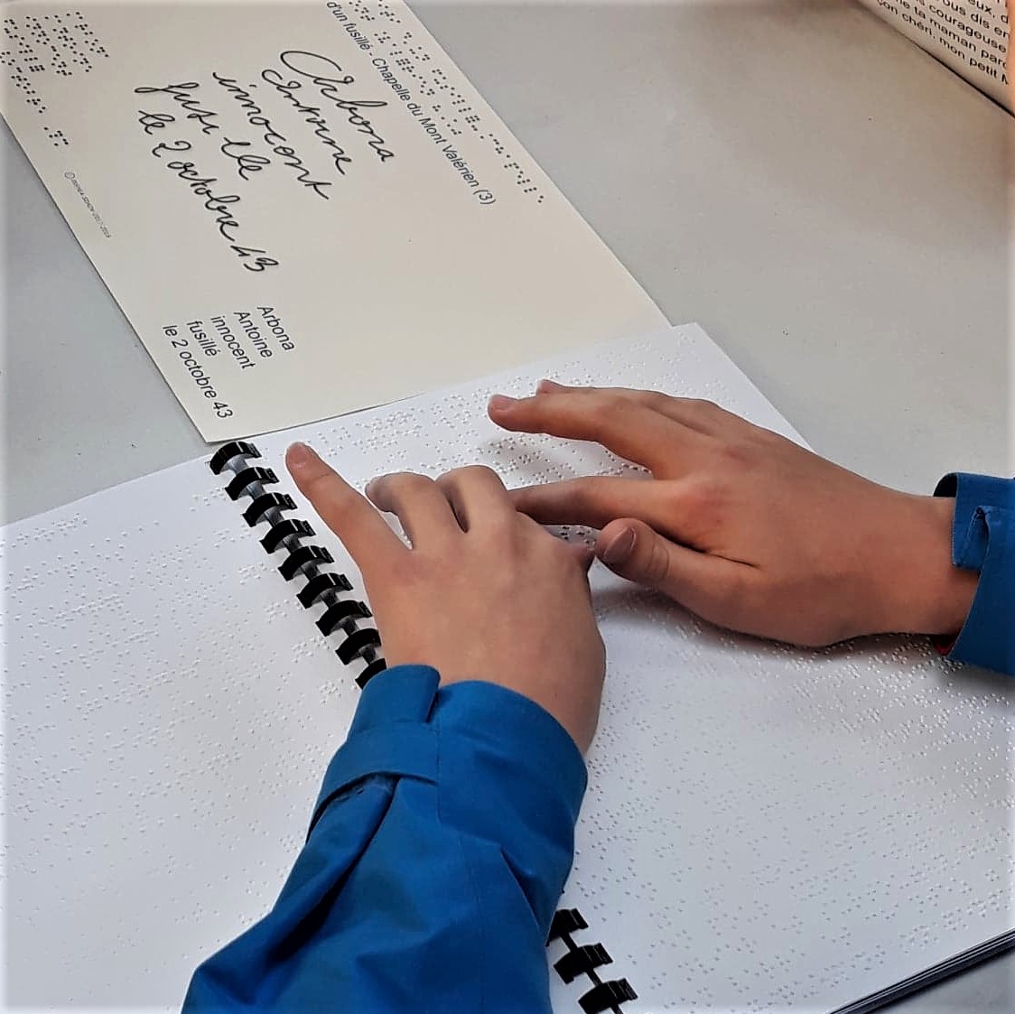Photos de 2 mains d'enfant en train de lire un cahier en braille.
