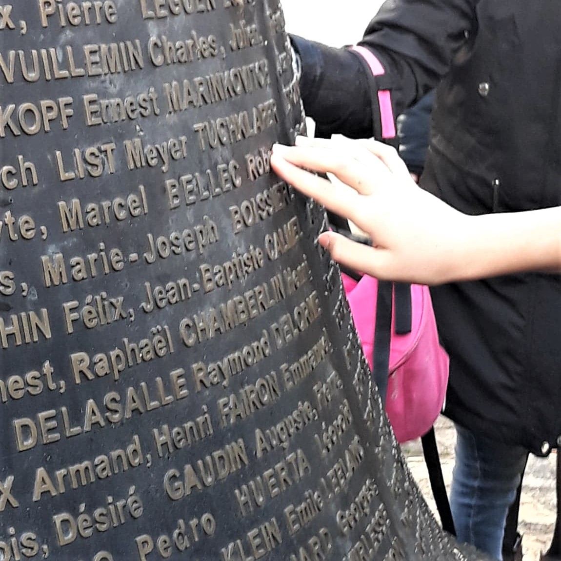 Photo représentant une main touchant les écritures en relief des noms des résistants et otages fusillés du Mont-Valérien.